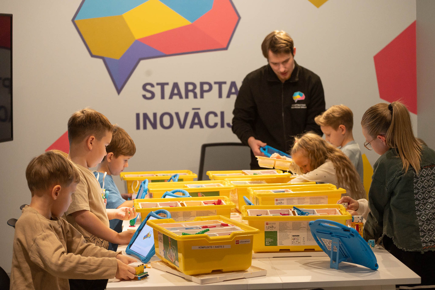 Bērni LEGO robotikas nodarbībā kopā ar pedagogu